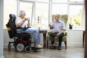 Male And Female Residents Sitting In Chairs and Talking In Retirement Home