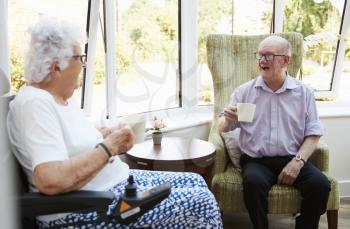 Male And Female Residents Sitting In Chairs and Talking In Retirement Home