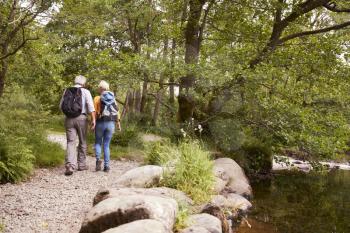 Rear View Of Senior Couple Hiking Along Path By River In UK Lake District