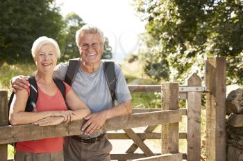 Portrait Of Senior Couple Hiking In Lake District UK Looking Over Wooden Gate