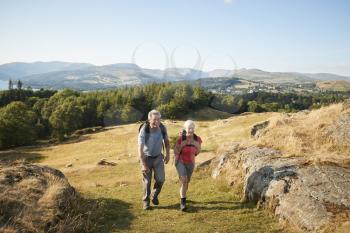 Senior Couple Climbing Hill On Hike Through Countryside In Lake District UK Together