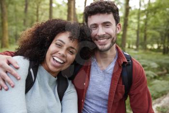 A young adult mixed race couple laughing to camera during a hike in a forest, portrait