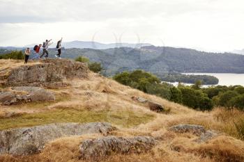 A group of five mixed race young adult friends arrive at summit with arms in the air after a mountain hike