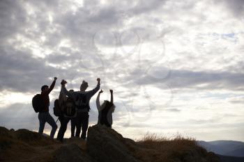Silhouettes of five young adult friends celebrating at the summit after a mountain hike, back view