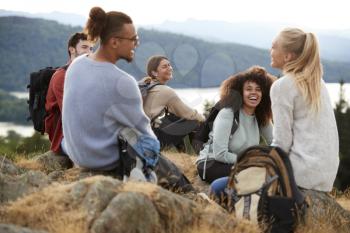 Five young adult friends sit talking at the summit after a mountain hike, close up