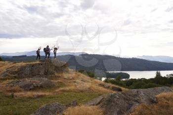 A group of five happy young adult friends cheer with their arms in the air at the summit after a mountain hike