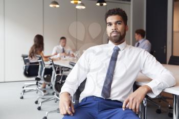 Portrait Of Businessman In Modern Boardroom With Colleagues Meeting Around Table In Background
