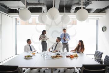 Businessmen And Businesswomen Meeting In Modern Boardroom Over Working Lunch