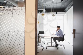 Businessman Working On Laptop At Boardroom Table Viewed Through Meeting Room Door