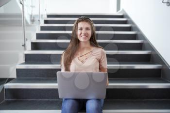 Portrait Of Female High School Student Sitting On Staircase And Using Laptop