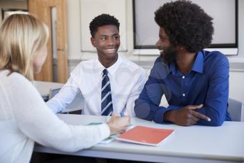 Father And Teenage Son Having Discussion With Female Teacher At High School Parents Evening