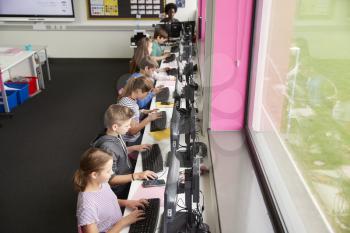 Line Of High School Students Working at Screens In Computer Class With Female Teacher In Background Shot From High Angle