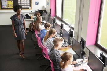 Female Teacher Supervising Line Of High School Students Working at Screens In Computer Class