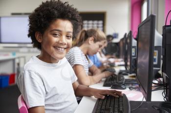 Portrait Of Smiling Male Pupil Sitting In Line Of High School Students Working at Screens In Computer Class