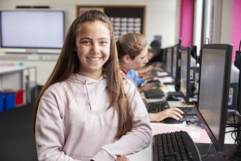Portrait Of Smiling Female Pupil Sitting In Line Of High School Students Working at Screens In Computer Class