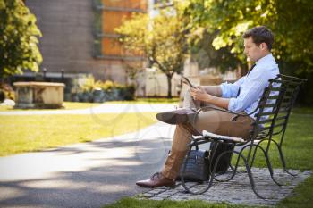 Businessman Outdoors Using Digital Tablet On Lunch Break In Park