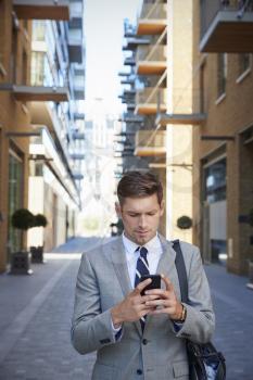 Businessman Walking To Work In City Looking At Mobile Phone