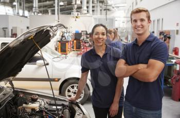 Two apprentice mechanics looking to camera beside a car