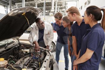 Mechanic instructing trainees around the engine of a car