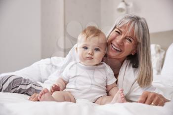 Grandmother Lying In Bed At Home Looking After Baby Grandson