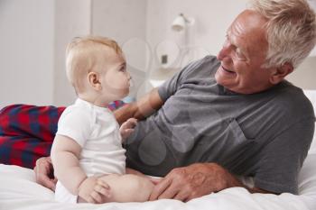 Grandfather Lying In Bed At Home Looking After Baby Grandson
