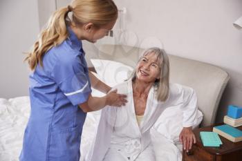 Nurse Helping Senior Woman Out Of Bed On Home Visit