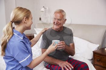 Nurse Making Home Visit To Senior Man In Bed