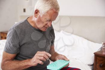 Senior Man Sitting On Bed At Home Taking Medication