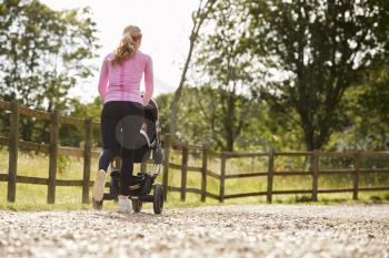 Rear View Of Mother Exercising By Running And Pushing Baby Buggy