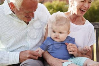 Grandparents Sitting On Seat In Garden With Baby Grandson
