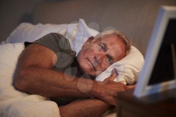 Sad Senior Man Lying In Bed Looking At Photo Frame