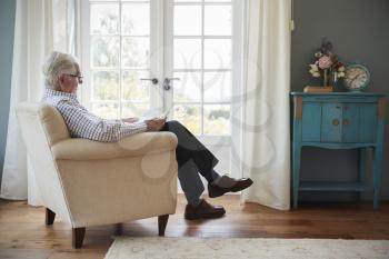 Senior man sitting in an armchair reading a book at home