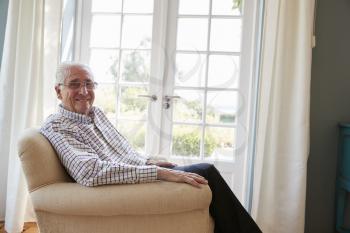 Senior man sitting in an armchair turns smiling to camera