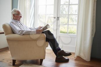 Senior man sitting in an armchair reading newspaper at home