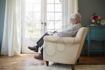 Senior man sitting in an armchair doing  crossword, side view
