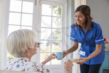 Nurse serving tea to senior woman at home, close up