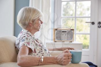 Senior woman drinking tea and listening to radio at home