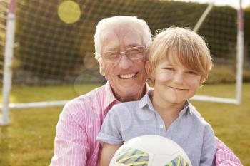 Senior man and grandson holding ball smiling at camera