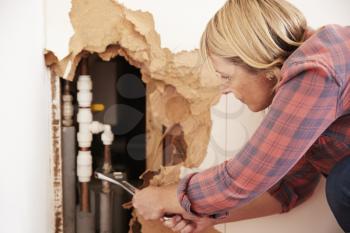 Middle aged woman repairing burst water pipe with a wrench