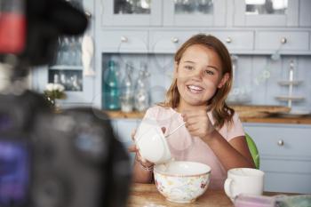 Pre-teen girl video blogging in kitchen mixing ingredients