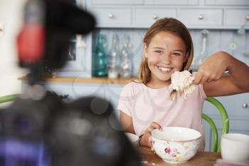 Young girl video blogging in kitchen showing spoon of dough