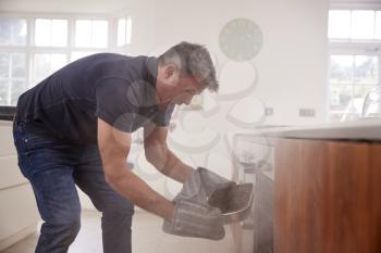 Middle aged man opening smoke filled oven in the kitchen