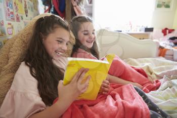 Two Sisters Reading Book Sitting On Bed Together