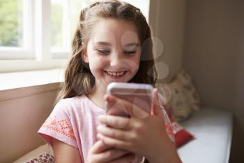 Smiling Girl Sitting On Window Seat Playing Game On Mobile Phone