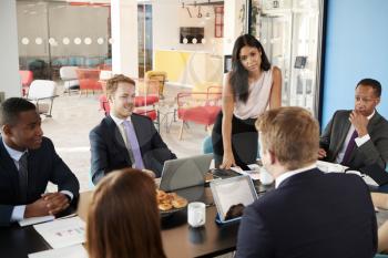 Female boss stands listening to colleagues at team meeting