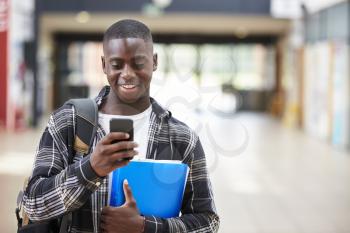 Male College Student Reading Text Message On Mobile Phone