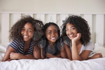 Portrait Of Three Teenage Sisters Lying On Bed At Home