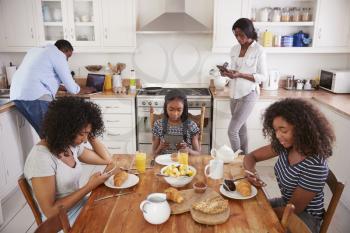 Family Sitting Around Breakfast Table Using Digital Devices