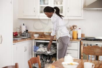 Woman Clearing Breakfast Table And Loading Dishwasher