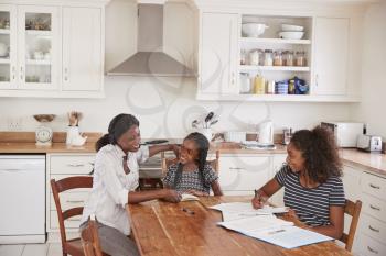 Mother Helping Two Daughters Sitting At Table Doing Homework